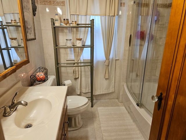 full bathroom featuring combined bath / shower with glass door, vanity, tile patterned floors, toilet, and tile walls