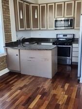 6410 N Hoyne Ave Unit 3E, Chicago, IL 60645 - kitchen featuring appliances with stainless steel finishes, dark countertops, dark wood-style flooring, and a peninsula