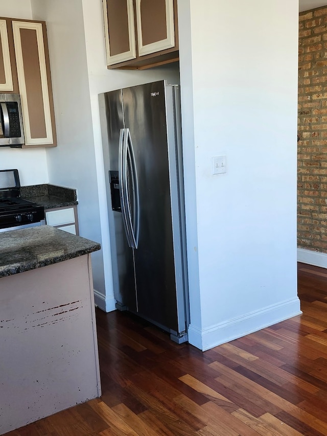 kitchen with appliances with stainless steel finishes, dark wood-type flooring, cream cabinets, and brick wall