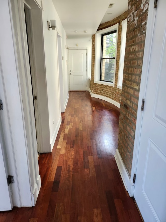 corridor with dark hardwood / wood-style floors and brick wall