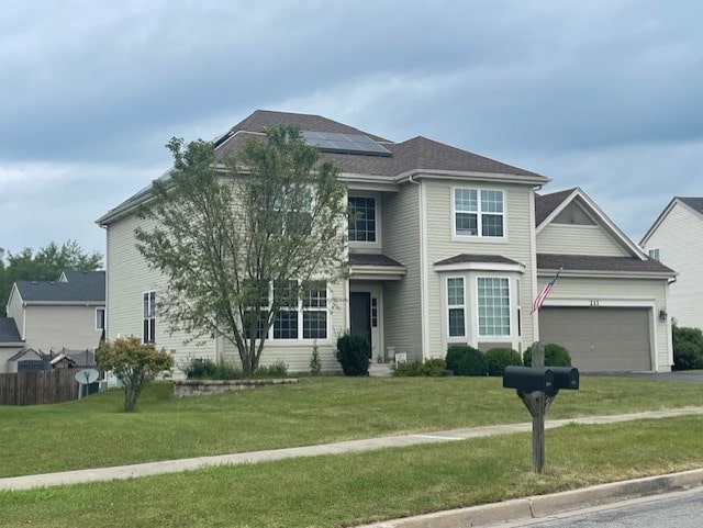 view of front facade featuring a garage, roof mounted solar panels, aphalt driveway, and a front yard