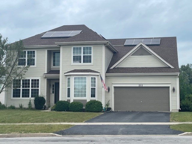 view of front of home featuring a shingled roof, an attached garage, a front lawn, solar panels, and driveway