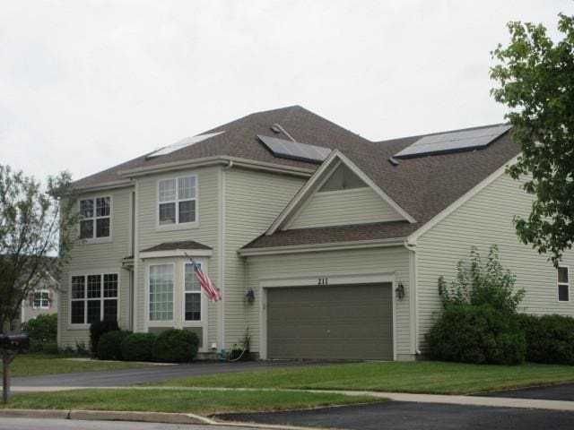 view of front of property featuring a garage, roof mounted solar panels, roof with shingles, and aphalt driveway