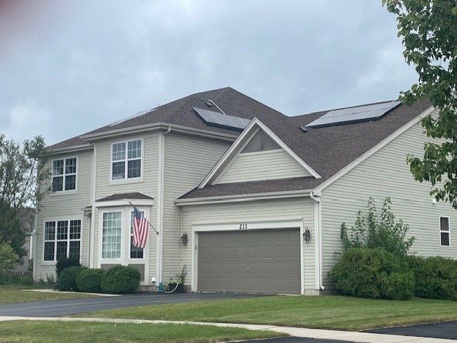 view of front of property with a shingled roof, solar panels, a front lawn, and aphalt driveway