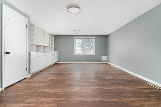 spare room with built in shelves and dark hardwood / wood-style floors