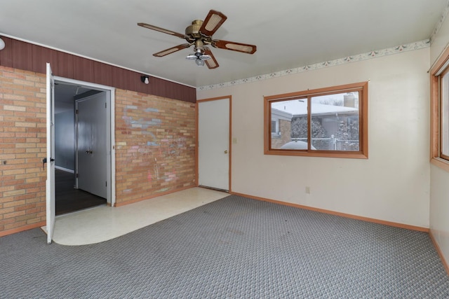 carpeted empty room with ceiling fan and brick wall