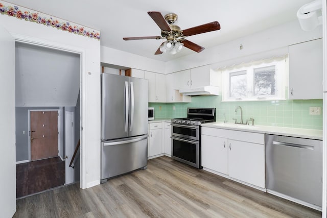 kitchen featuring custom exhaust hood, white cabinets, sink, light wood-type flooring, and stainless steel appliances