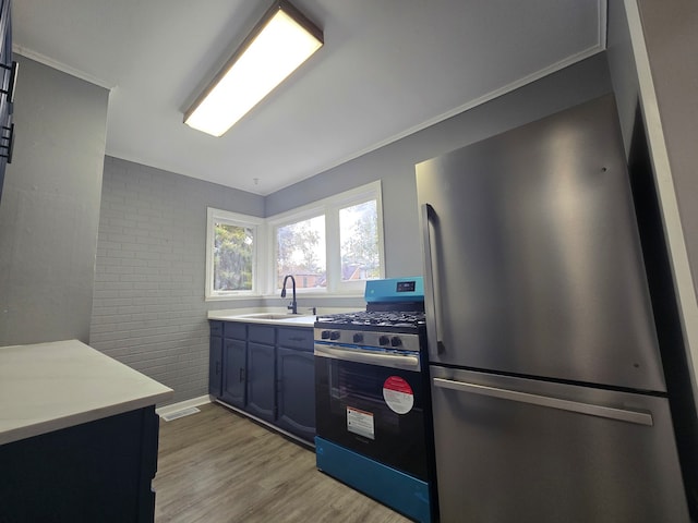 kitchen featuring ornamental molding, sink, brick wall, appliances with stainless steel finishes, and light hardwood / wood-style floors