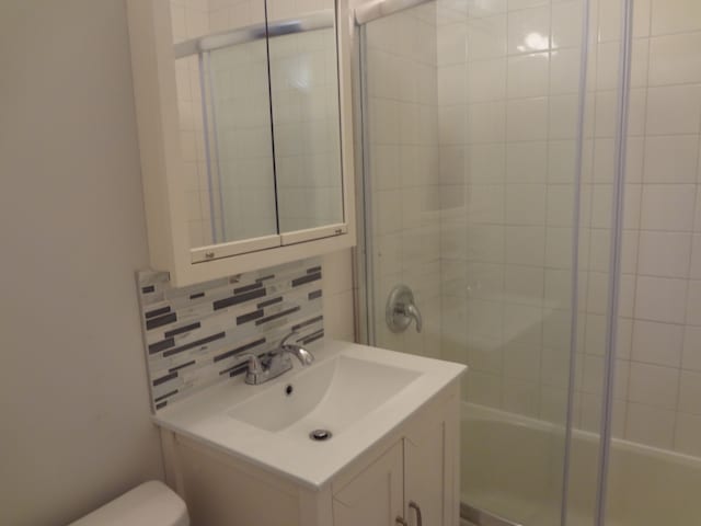 bathroom with a shower with door, toilet, decorative backsplash, and vanity