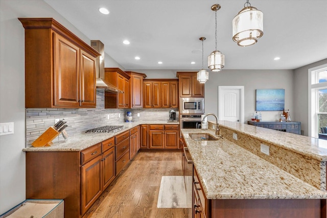 kitchen with light stone counters, wall chimney range hood, hanging light fixtures, and appliances with stainless steel finishes