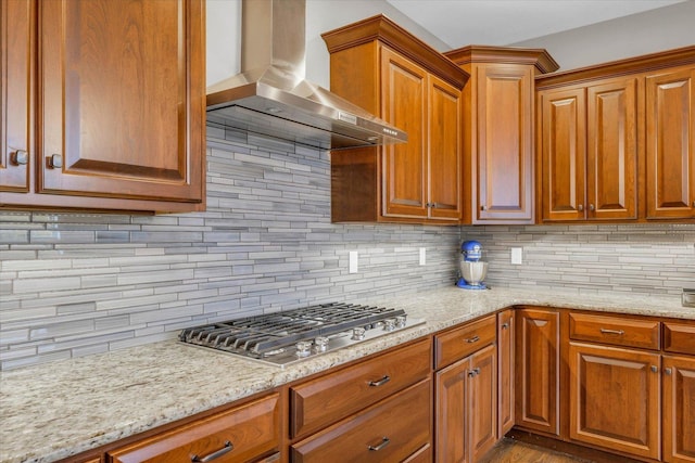 kitchen featuring decorative backsplash, light stone counters, stainless steel gas cooktop, and wall chimney exhaust hood