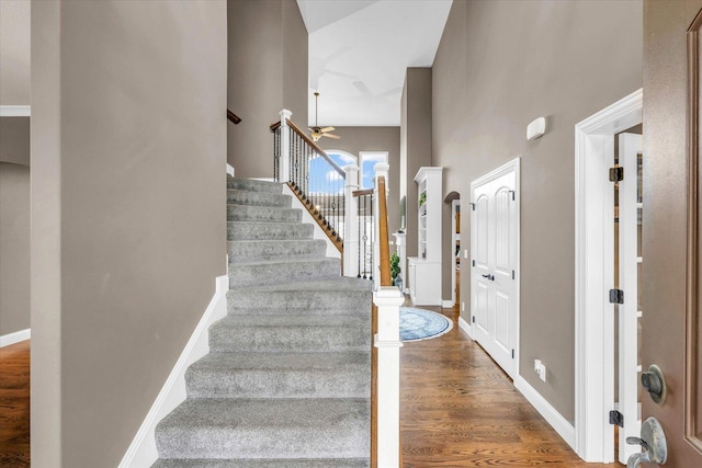 stairs with ceiling fan, a towering ceiling, and hardwood / wood-style flooring