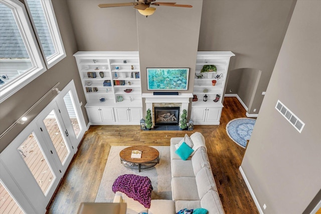 living room with a towering ceiling, dark hardwood / wood-style flooring, ceiling fan, and a healthy amount of sunlight