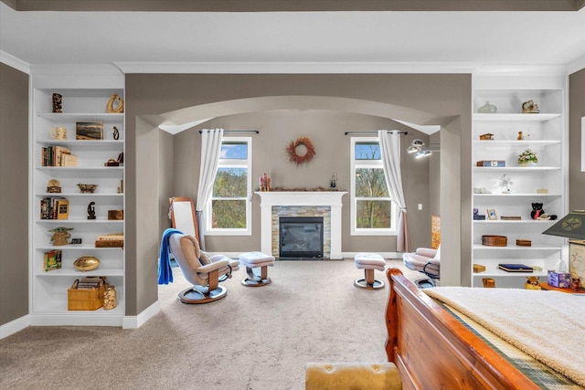 carpeted bedroom featuring a stone fireplace, crown molding, and multiple windows