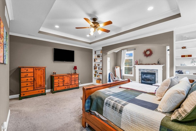 bedroom with ceiling fan, a raised ceiling, light colored carpet, a fireplace, and ornamental molding