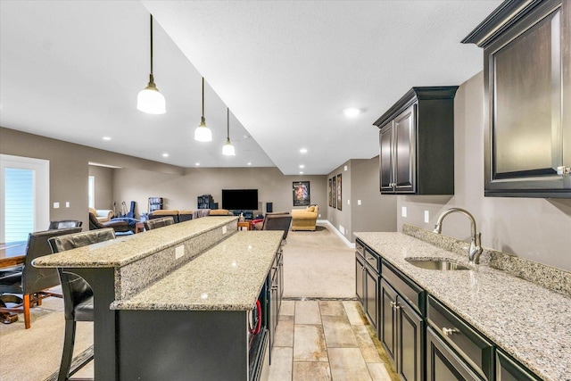 kitchen with a kitchen breakfast bar, light stone counters, sink, a kitchen island, and hanging light fixtures