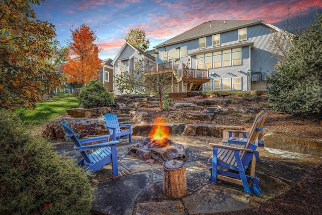 back house at dusk featuring a wooden deck, a patio area, and a fire pit