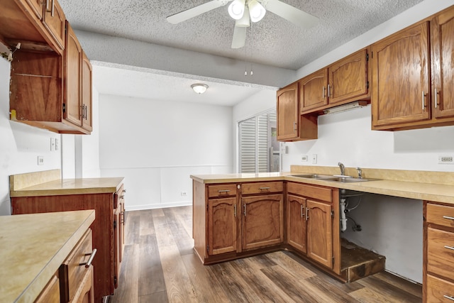 kitchen with kitchen peninsula, ceiling fan, dark hardwood / wood-style flooring, a textured ceiling, and sink