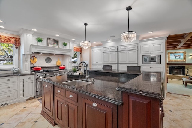 kitchen featuring appliances with stainless steel finishes, sink, white cabinets, hanging light fixtures, and a center island with sink