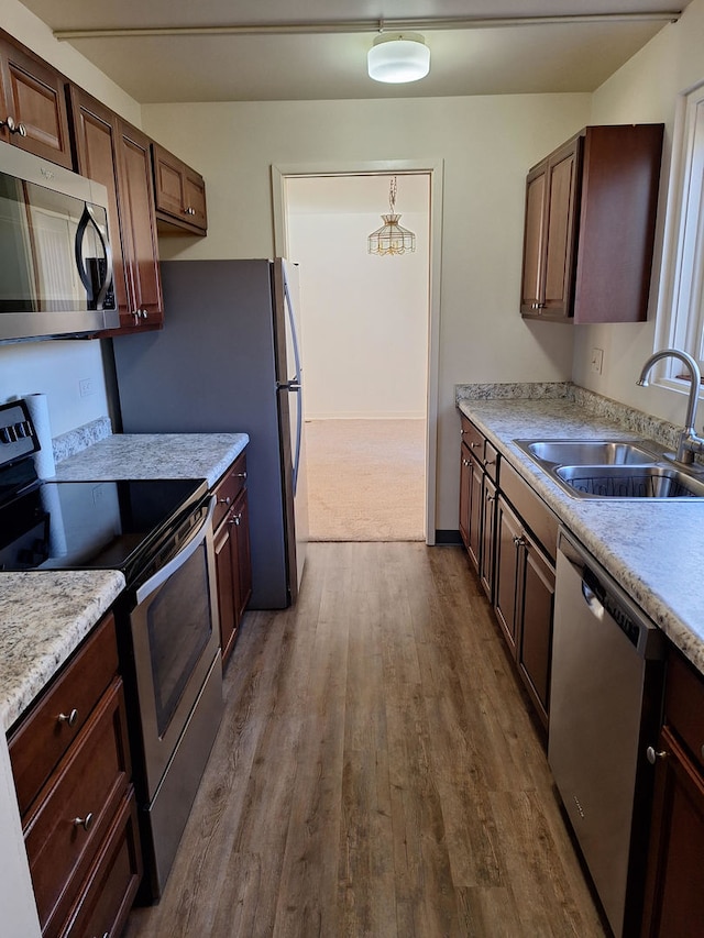 kitchen featuring wood-type flooring, appliances with stainless steel finishes, sink, dark brown cabinetry, and decorative light fixtures