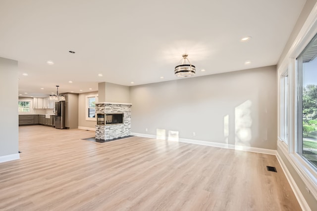 unfurnished living room with light hardwood / wood-style flooring, a multi sided fireplace, and an inviting chandelier