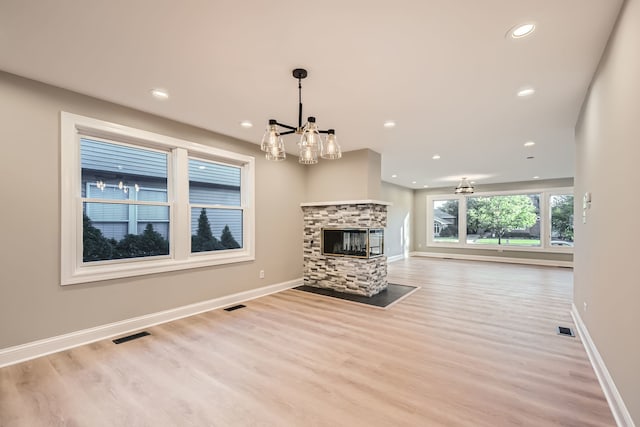 unfurnished living room featuring a multi sided fireplace, a notable chandelier, and light wood-type flooring