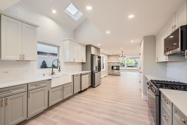 kitchen featuring gray cabinets, appliances with stainless steel finishes, vaulted ceiling with skylight, sink, and light hardwood / wood-style floors