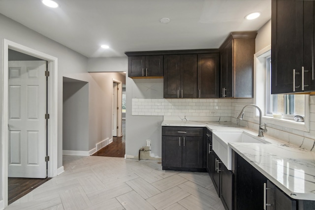 kitchen with dark brown cabinetry, sink, tasteful backsplash, and light stone countertops