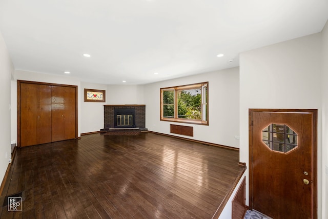 unfurnished living room with dark wood-type flooring and a brick fireplace