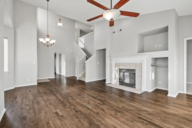 unfurnished living room featuring a tile fireplace, ceiling fan with notable chandelier, dark wood-type flooring, and a high ceiling