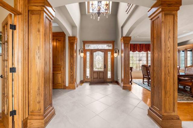 foyer with light tile patterned floors, ornamental molding, a high ceiling, ornate columns, and a notable chandelier