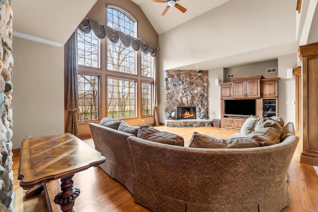 living room with light hardwood / wood-style floors, high vaulted ceiling, a fireplace, and ceiling fan