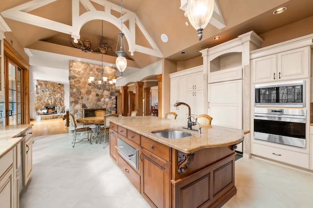 kitchen with stainless steel oven, a kitchen island with sink, a fireplace, pendant lighting, and light stone counters