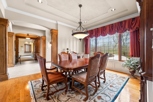 dining room with light hardwood / wood-style flooring, a tray ceiling, crown molding, and decorative columns