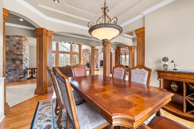 dining space featuring light hardwood / wood-style flooring, a healthy amount of sunlight, ornate columns, and a raised ceiling