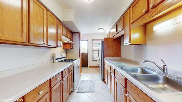 kitchen featuring sink, light tile patterned flooring, white gas range, and stainless steel refrigerator