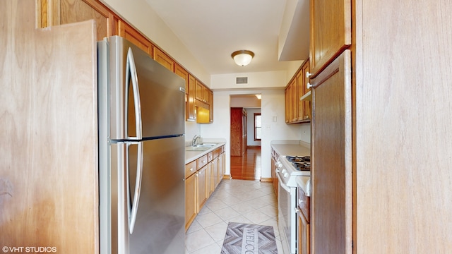 kitchen featuring sink, light tile patterned floors, white range, and stainless steel fridge