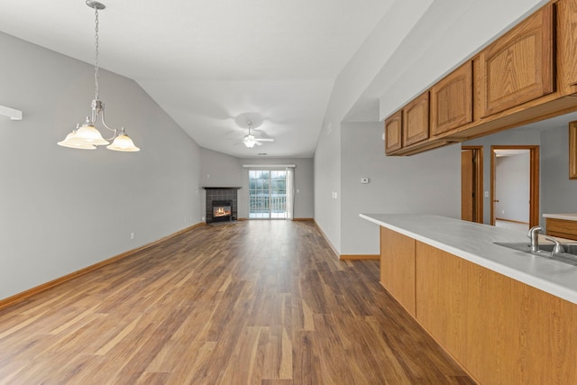 kitchen featuring dark wood-type flooring, ceiling fan with notable chandelier, hanging light fixtures, vaulted ceiling, and a fireplace