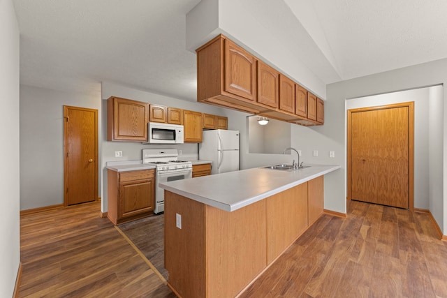 kitchen featuring kitchen peninsula, white appliances, dark hardwood / wood-style floors, and sink