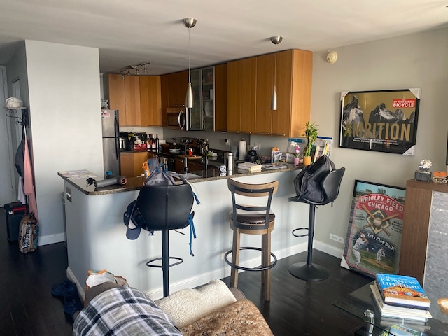 kitchen with kitchen peninsula, hanging light fixtures, a kitchen breakfast bar, stainless steel appliances, and dark wood-type flooring