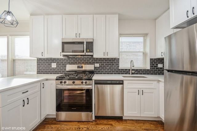 kitchen with dark wood-type flooring, stainless steel appliances, decorative light fixtures, and white cabinets