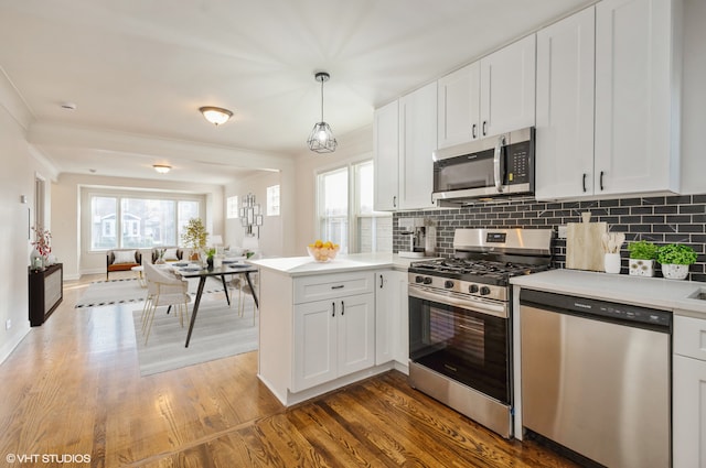 kitchen with appliances with stainless steel finishes, kitchen peninsula, white cabinetry, pendant lighting, and dark wood-type flooring