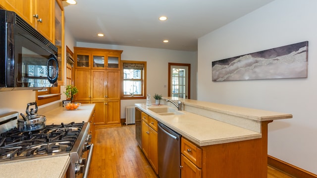 kitchen with radiator, sink, stainless steel appliances, an island with sink, and light wood-type flooring