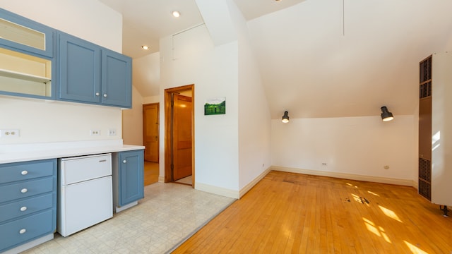 kitchen with blue cabinets, vaulted ceiling, fridge, and light hardwood / wood-style floors