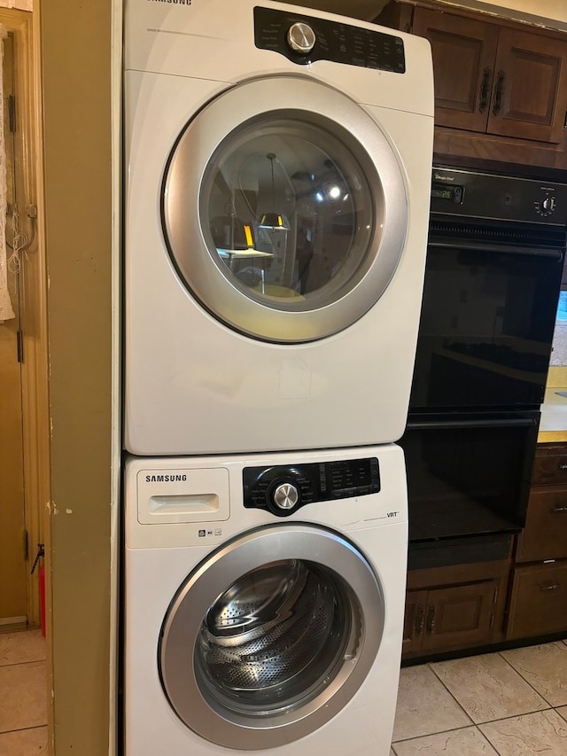 clothes washing area with light tile patterned floors and stacked washer and clothes dryer