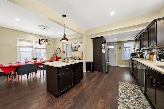 kitchen featuring a kitchen island, dark brown cabinets, dark hardwood / wood-style flooring, stainless steel appliances, and decorative light fixtures