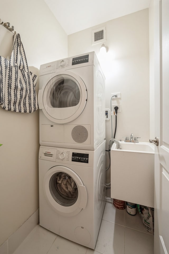 laundry area with stacked washer / dryer and light tile patterned floors