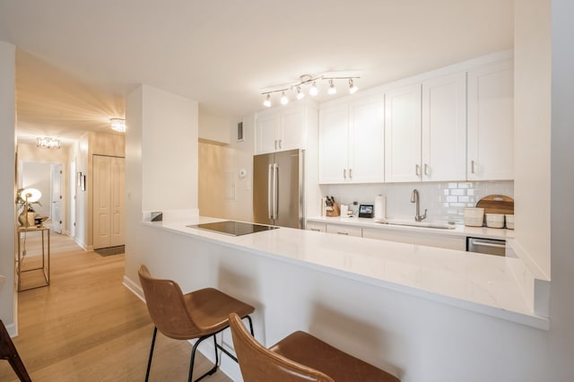 kitchen with kitchen peninsula, stainless steel appliances, sink, light wood-type flooring, and white cabinetry