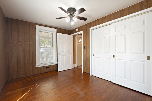 unfurnished bedroom with a closet, wood walls, dark hardwood / wood-style floors, and ceiling fan