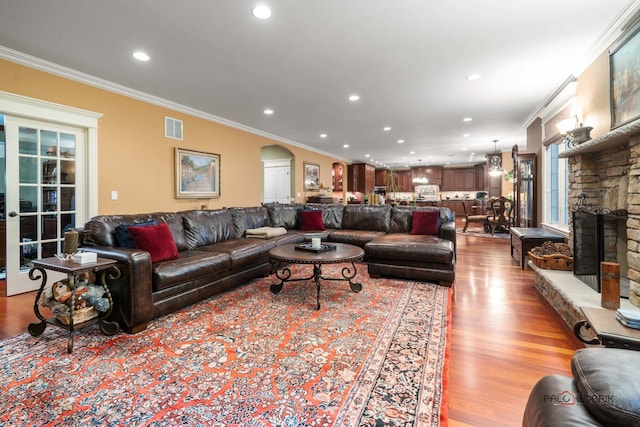 living room featuring ornamental molding, light hardwood / wood-style flooring, and a stone fireplace